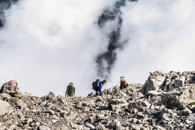 Drei Personen steigen auf zum Hocheck auf der Watzmanntour, Der Aufstieg ist sehr Felsig und im Hintergrund verdecken die Wolken die Aussicht auf umliegende Berge